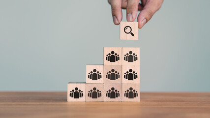 Hand places a wooden cube block with a magnifying glass icon with people team icon, symbolizing...