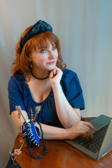 A beautiful young woman is working or playing or shopping on a laptop in a stylish modern dress and a hair band in the shape of the Russian national kokoshnik headdress