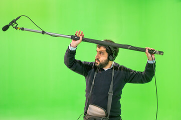 Boom microphone operator testing sound at TV studio on green key chroma background. High quality photo