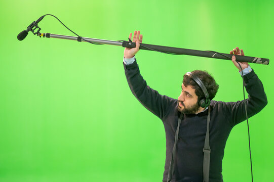 Boom microphone operator testing sound at TV studio on green key chroma background. High quality photo