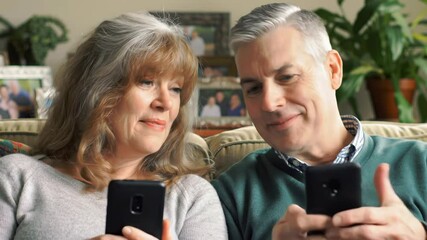 Mature couple using phones together at home on the couch - Powered by Adobe