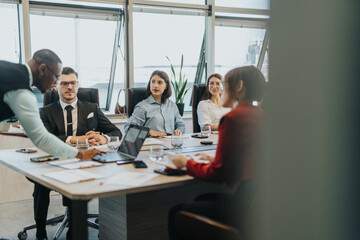 A diverse group of business people are gathered around a conference table, actively discussing and...