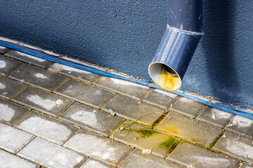 There is a noticeable leak coming from a drain pipe onto the brick sidewalk