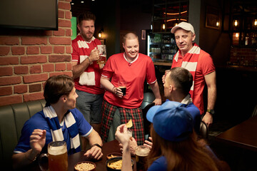Group of middle aged and young Caucasian men and women gathering in sports bar wearing soccer fan...