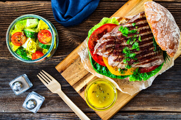 Takeaway sandwich with grilled beef steak and tomato served with fresh salad and vinaigrette sauce...