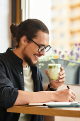 Young man enjoys matcha while freelancing in a cozy summer cafe environment