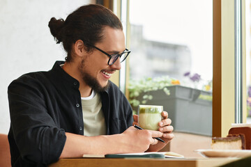 Young man enjoys remote work while sipping matcha and indulging in cake at a cozy cafe