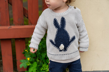 Innocence and wonder of childhood — cozy toddler in playful bunny sweater exploring outdoors,...