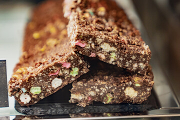 Stacked chocolate dessert bars with crunchy texture and colorful candy pieces on display in bakery or pastry shop, sweet baked treat