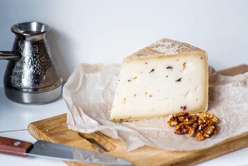 A piece of fresh, aged, natural farm cheese with walnuts on parchment on a wooden board. The quality of farm-fresh agricultural products.