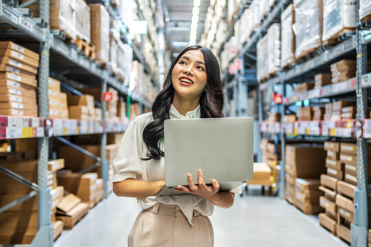 Engaging in meticulous inventory management, a young asian woman professional examines products while using a laptop computer, surrounded by organized shelves filled with boxes