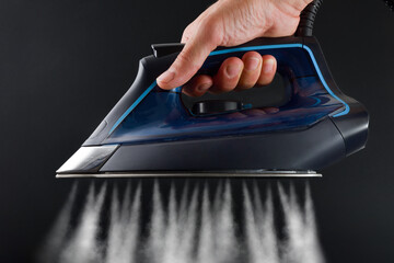 Hand operating steam iron and jets coming out dark background