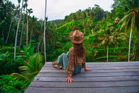 Happy carefree woman traveler wearing hat enjoying landscape of picturesque green rice terraces in Ubud, Bali island, exploring and traveling to beautiful destinations