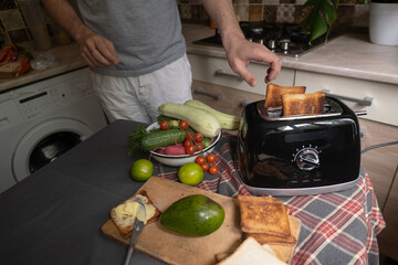 Man prepares toast with vegetables and avocado using a toaster quick and healthy morning breakfast...