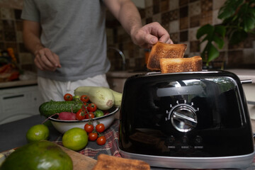 Man uses toaster to quickly prepare healthy breakfast with vegetables and greens simple morning...