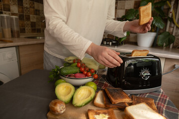 Home kitchen in the morning woman puts bread into toaster quick way to prepare a tasty breakfast and start the day right.