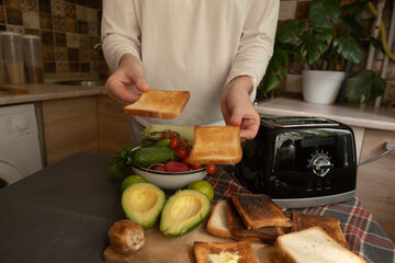 Morning in a cozy kitchen woman uses a toaster to prepare a healthy breakfast starting the day with simple home comfort.