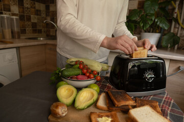 Home breakfast with toaster woman puts bread into appliance preparing toast for a sandwich quick and easy morning routine.
