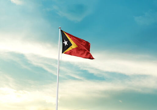 East Timor flag is waving on a tall flagpole among the clouds. East Timor national flag for independence day.