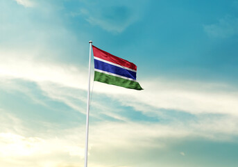 The Gambia flag is waving on a tall flagpole among the clouds. The Gambia national flag for independence day.