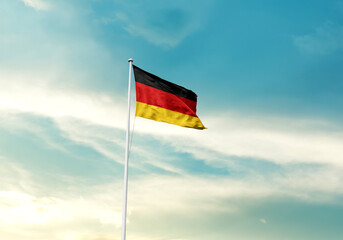 Germany flag is waving on a tall flagpole among the clouds. Germany national flag for independence day.