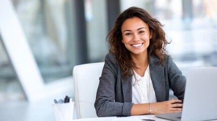 Fototapeta premium Confident young Hispanic woman in professional attire seated at a clean desk, working online with positive energy.