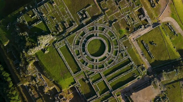 A mesmerizing top-down drone shot spins while descending, creating a hypnotic vortex effect over the circular stone foundations of an ancient Inca tower at the Saqsaywaman ruins.
