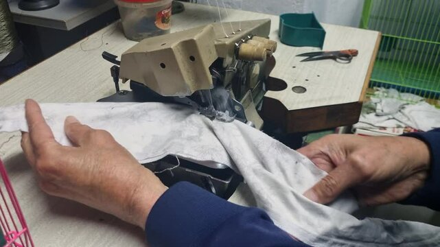 An elderly hand guides a piece of textile through an old sewing machine, capturing the rhythm of everyday labor in 1950s Yugoslavia