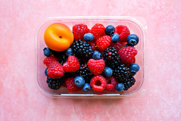 A container of fresh mixed berries and an apricot