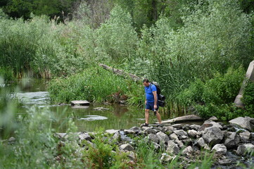 Obraz premium A man crosses a river on rocks with a backpack.