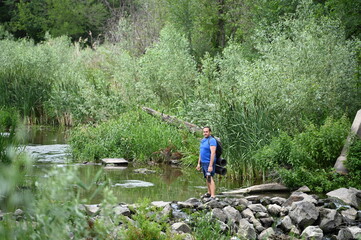 Obraz premium A man crosses a river on rocks with a backpack.