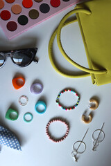 Green bag, various colorful jewelry, sunglasses, hair accessories and colorful make up on white background. Flat lay.