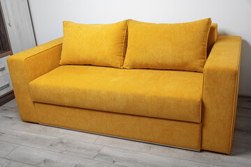 A modern yellow fabric sofa with two large cushions is placed in a bright, minimalistic living room...