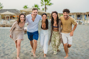 Five happy friends walking on the beach at sunset