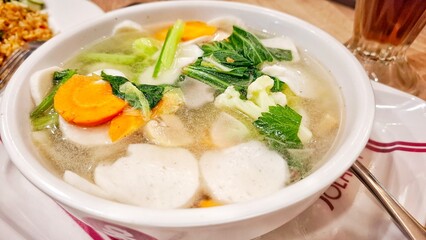 A capcay dish served in a white bowl with various vegetables and meats and a soup typical of Indonesian cuisine.