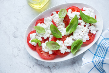 Caprese with cottage cheese, tomatoes and fresh basil on a white stone background, horizontal shot, high angle view