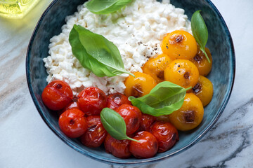 Cottage cheese caprese with roasted tomatoes and fresh green basil served in a blue bowl, horizontal shot, middle closeup