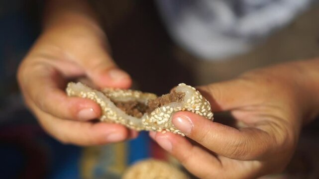 A woman's hand eating Onde-onde or traditional sesame balls filled with sweet mung bean paste, an Asian snack