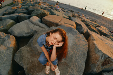 lifestyle woman in modern boho-western denim street style sitting relaxed on large beach rocks with...