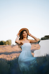 Woman in white dress and hat plays piano in lavender field during sunset