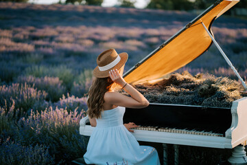 Woman plays piano in lavender field at sunset dressed in white and wearing a hat