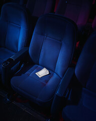 Fototapeta premium Empty cinema seat with ticket on armrest under dim lighting 