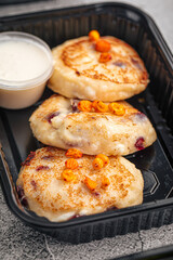 Cottage cheese pancakes with berries and sour cream in black container