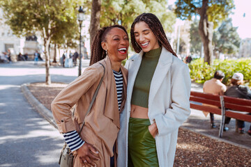 Mother and daughter are sharing a laugh in a sunny city park, enjoying each other's company. Two...