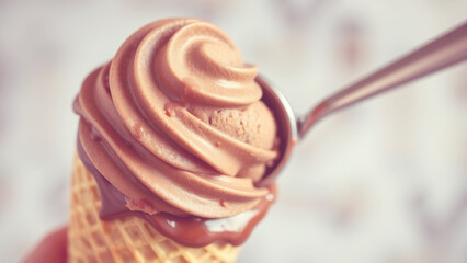 Fototapeta premium Swirling chocolate soft serve ice cream cone with spoon held above at a sunny outdoor setting