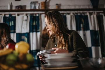 A woman arranges dishes while standing indoors, surrounded by a convivial and inviting atmosphere....