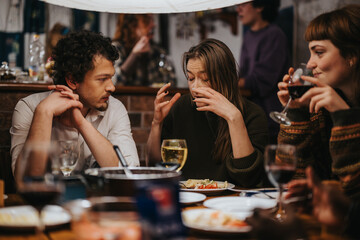 A diverse group of friends gathered indoors around a table, enjoying food, drinks, and conversations. The atmosphere is warm and convivial, showcasing friendship and relaxation in a cozy space.