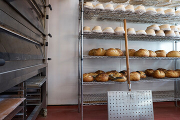 Freshly baked sourdough loaves cooling on racks in bakery with banneton baskets for proving above, oven and paddle