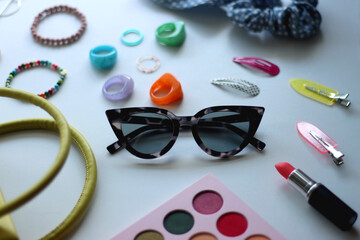 Green bag, various colorful jewelry, sunglasses, hair accessories and colorful make up on white background. Selective focus.