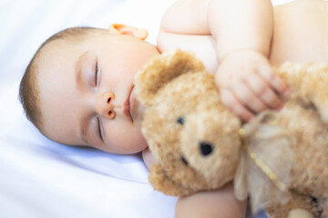 Cute baby with teddy bear toy in blurred foreground, sleeping on white sheet. close-up of baby
